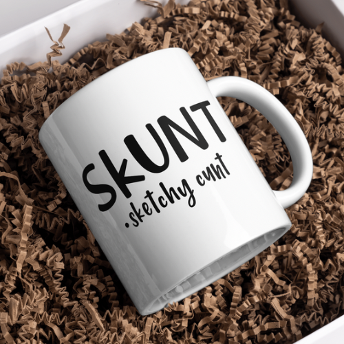 White ceramic skunk mug with bold black text "SKUNT sketchy cunt" in protective packaging