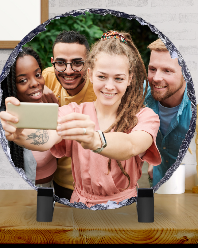 Circle Photo Slate 15x15cm with glossy finish featuring a printed photo of four friends taking a selfie, displayed on a wooden table with black stand feet